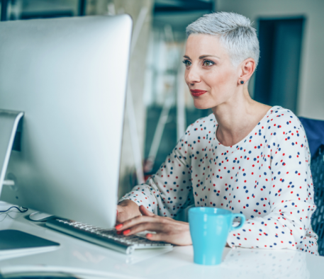 Caucasian woman with short cut, white hair, sitting at desk looking at computer